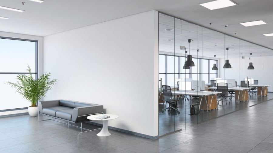Modern office lobby with sofa, plant and glass-walled workspace with desks and chairs