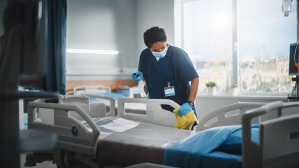 Nurse wearing mask and gloves cleaning a hospital bed in a patient room
